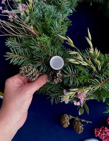 Handverzieren Sie den Kranz mit Tannenzapfen und Blumen.