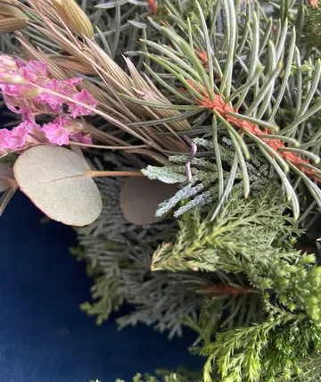 Gemischtes Laub mit rosa Blüten auf blauem Hintergrund.