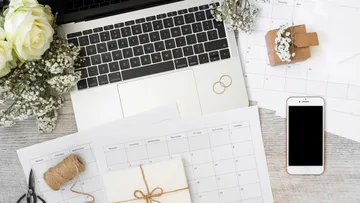 Wedding planning on laptop with calendars and flowers.