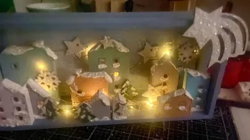 Wooden miniature snowy village with lights inside shadow box.