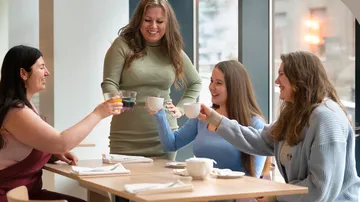 Vier Frauen toasten drinnen Getränke an einem Tisch.