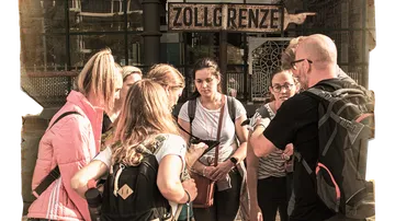 Group of people talking near 'Zollgrenze' sign.