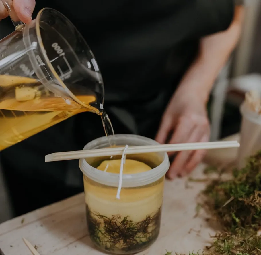 Pouring wax into candle mold on table.