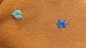 Blaue Blumen, gestickt auf orangefarbenem Stoff.