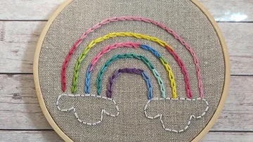 Regenbogenstickerei in einem Holzrahmen auf Stoff.