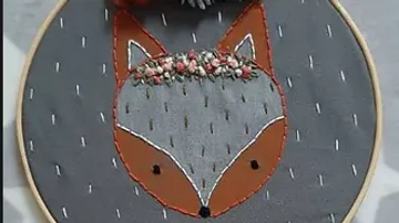 Fuchsstickerei mit Blumenkranz auf Stoff.
