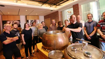 Group gathered around brewing equipment in a brewery.