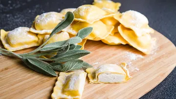 Ravioli and sage leaves on wooden board.