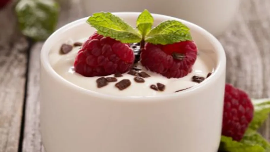 Yogurt topped with raspberries and mint on table.