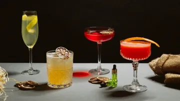 Vier elegante Cocktails mit Beilagen auf einem Tisch.