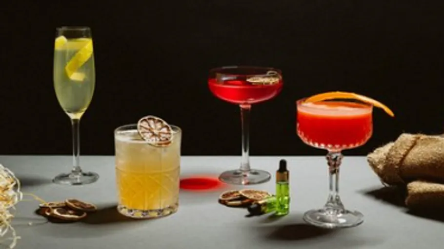 Four elegant cocktails with garnishes on a table.