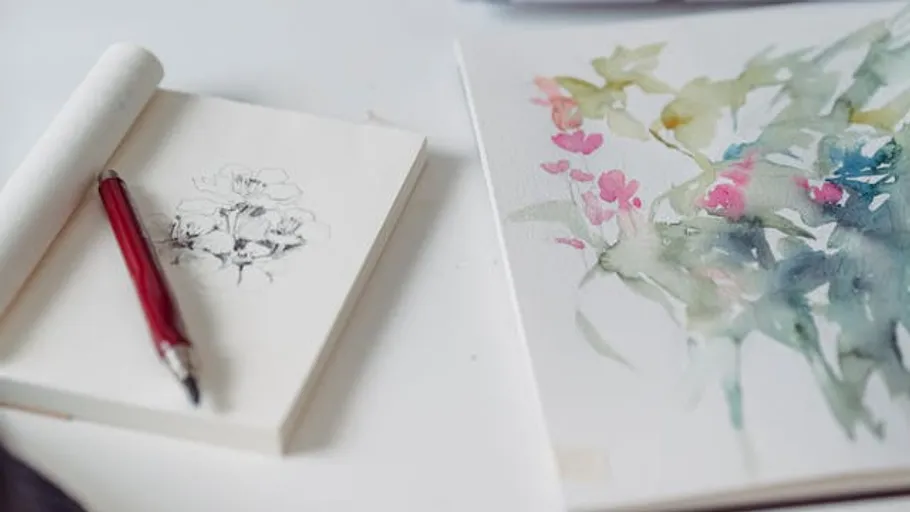 Sketchbook and watercolor painting on table.