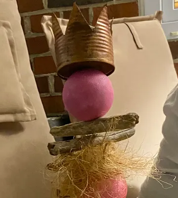 Holzskulptur mit rosafarbenen Kugeln, gekrönte Blechdose.