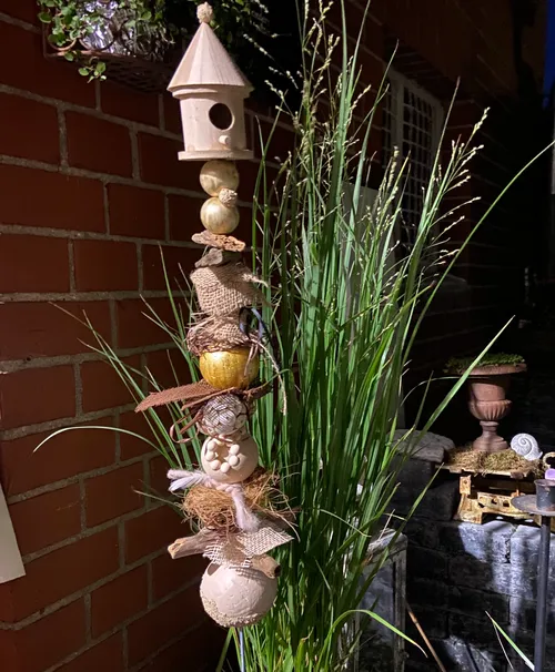 Decorative birdhouse with plants by brick wall.