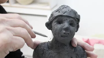 Hands sculpting clay figure in studio.