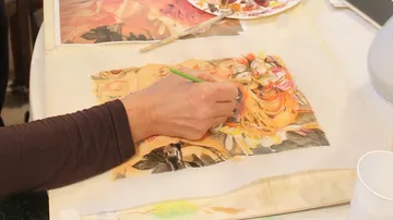 Person painting floral art on textured paper.