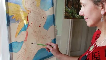 Woman painting an angel on canvas indoors.