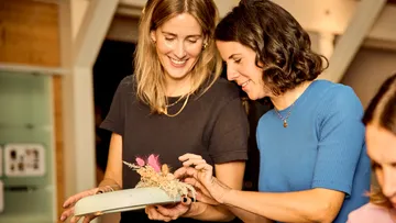 Two women arranging dried flowers together.