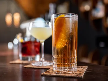 Cocktails auf Untersetzern, vor dunkler Bar-Hintergrund.