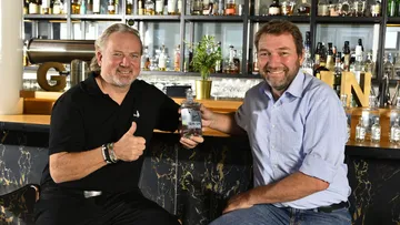 Two men smiling at a bar, holding gin bottle.