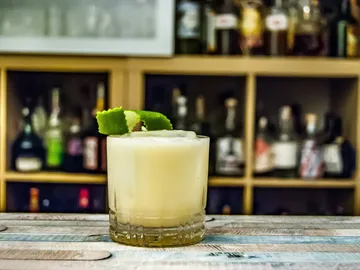 A cocktail is on a table in front of a bar.