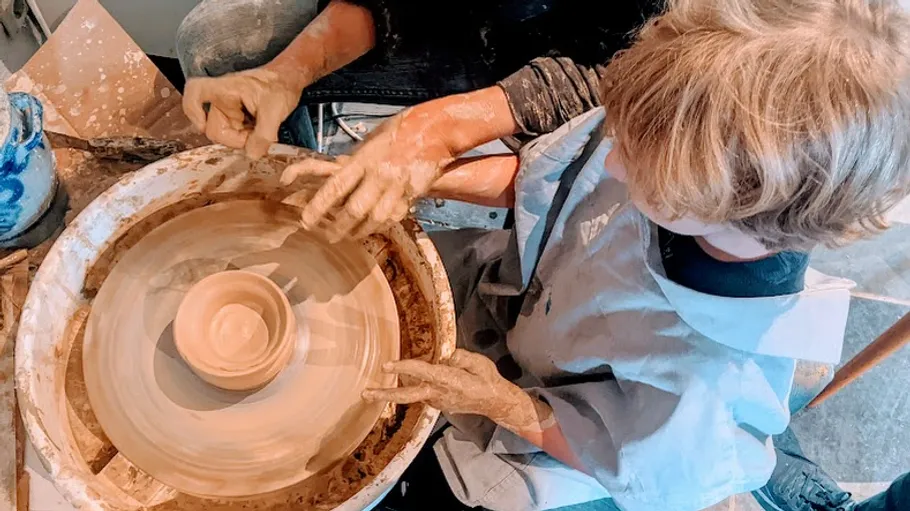 Child learning pottery with spinning wheel.