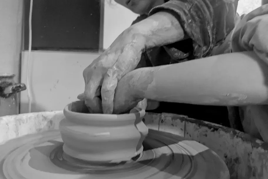 Hands shaping clay on pottery wheel.