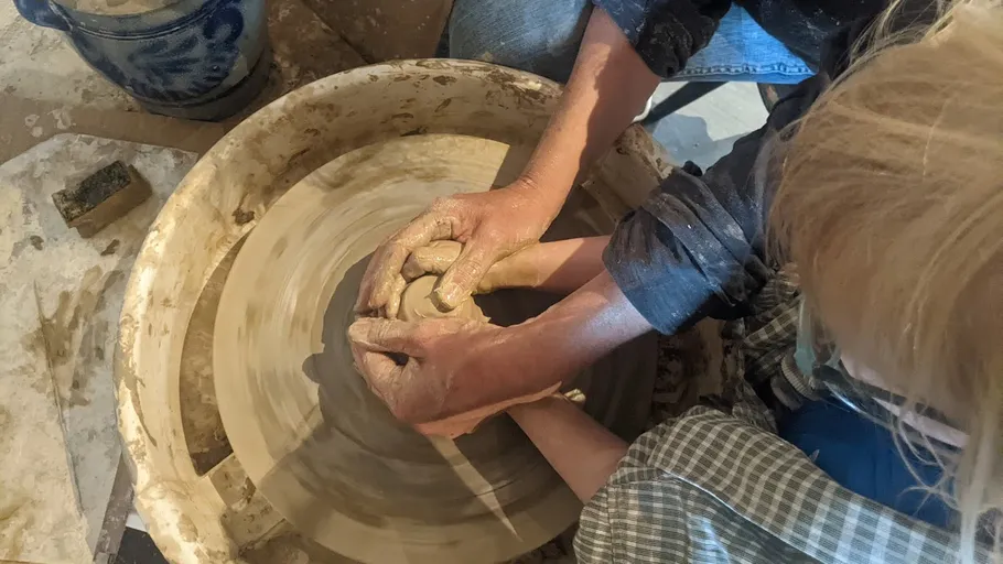 Adult and child shaping clay on pottery wheel.