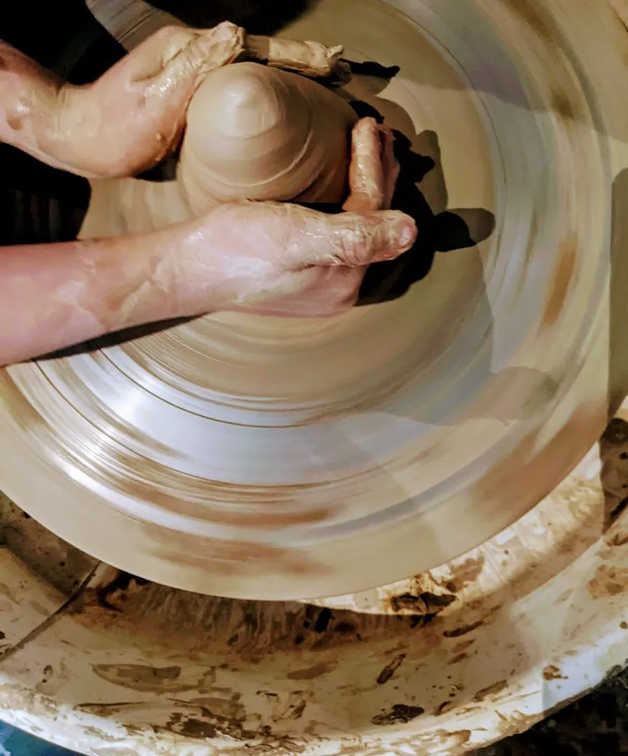 Hände formen Ton auf einer Töpferscheibe.