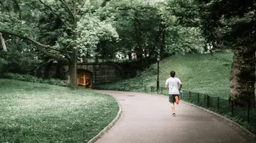 Person, die auf einem Parkweg, umgeben von viel Grün, joggt.