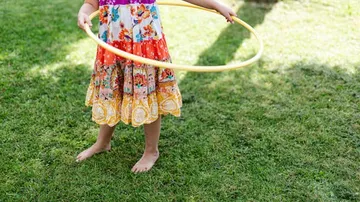 Child in colorful dress with hula hoop.