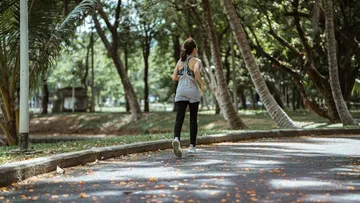 Person, die auf einem von Bäumen umgebenen Parkweg joggt.