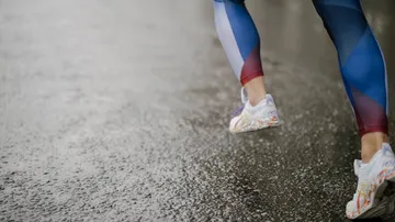 Person, die in Leggings auf nassem Bürgersteig läuft.