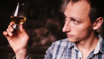 Man inspecting glass of whiskey indoors.