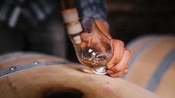 Hand haltend Glas in der Nähe eines Holzfasses.