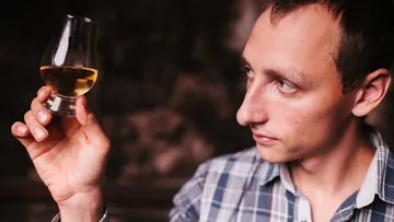 Mann untersucht ein Glas Whiskey genau.