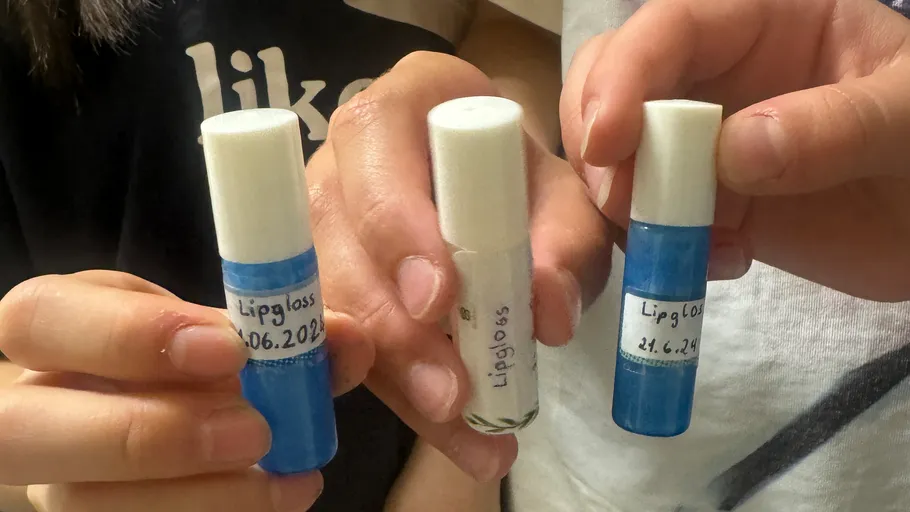 Three hands holding labeled lip gloss tubes.