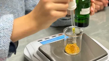 Person, die eine Pipette benutzt, um Öl in den Becher zu füllen.