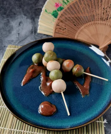 Dango skewers with sauce on blue plate, fan background.