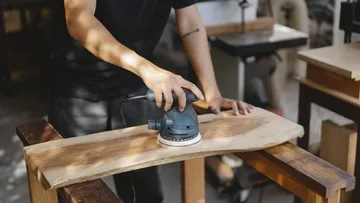 Person, die in der Werkstatt ein Holzbrett schleift.