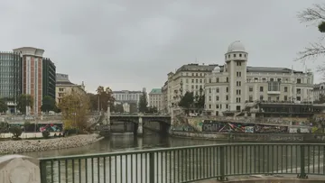 River flows under bridge with buildings and graffiti.