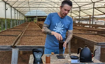Man brewing coffee in greenhouse setting.