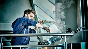 Person brewing beer in industrial brewery.