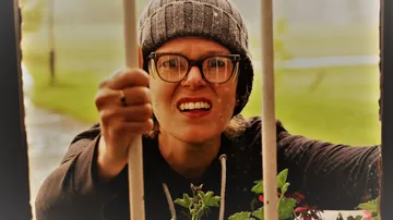 Person in hat looking through bars with plants.