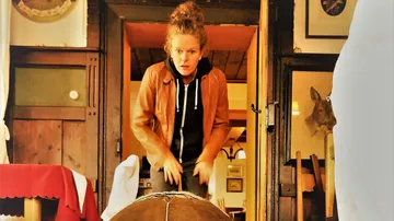 Person in brown jacket playing a large drum.