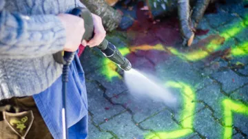 Person using pressure washer on graffiti-covered pavement.