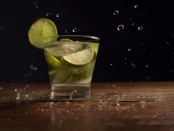 Ein Glas mit Limetten spritzt auf einer Holzoberfläche.