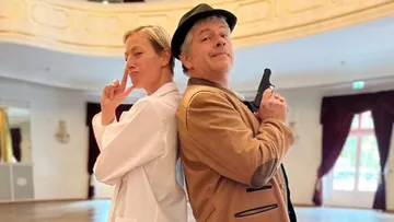 Two people posing back-to-back indoors, playfully.