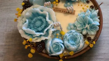 Decorative blue floral candle with flowers, pinecones, and label.
