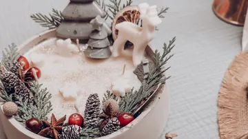 Festive candle with pinecones and reindeer figurine.